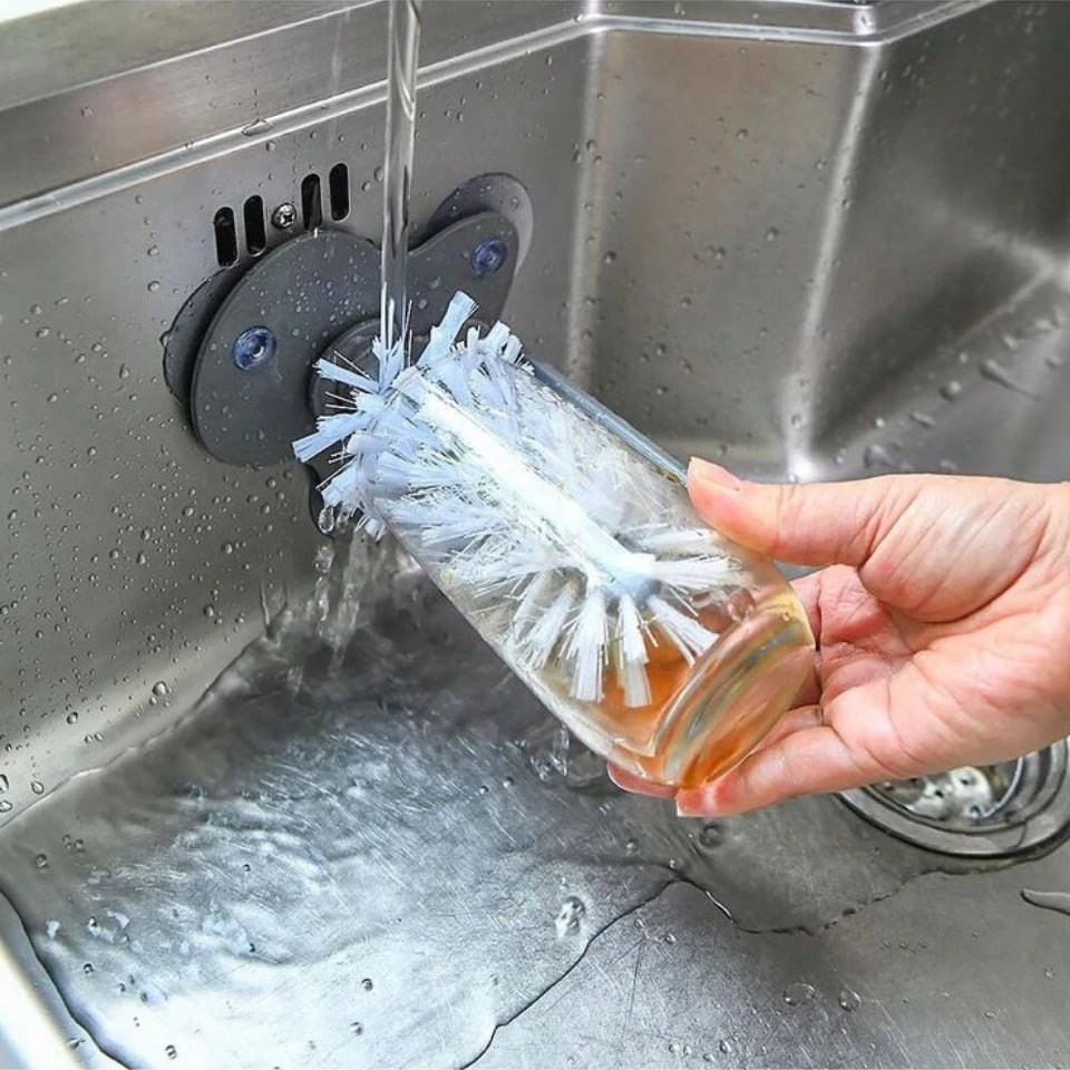 Person using a bottle brush to clean a glass bottle under running water in a sink.